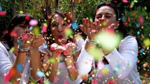 A group of people throwing and blowing confetti in the air outside.